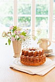A Bundt cake with icing sugar on a table in front of a window