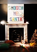 Christmas decorations in interior with fireplace; hand-crafted picture on wall with letters made from colourful woollen yarn, original floor lamp and wooden Christmas tree