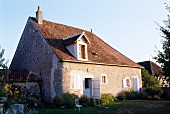 Altes, französiches Bauernhaus mit weissen Fensterläden an einstöckiger, schlichter Natursteinfassade