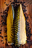 Smoked mackerel fillets on a pine wood board surrounded by peppercorns