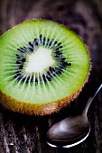 Half a kiwi and a spoon on a wooden surface
