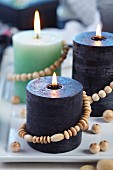 Verschiedenfarbige Kerzen mit Holzperlenkette dekoriert