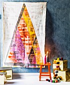 Artistic wall hanging of stylised Christmas tree on grey wall above presents wrapped in gold paper and lit candles
