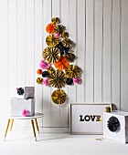 Stylised Christmas tree made from various colourful paper rosettes on white board wall and presents wrapped in white on floor and side table