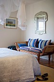 Antique ottoman bench with striped cushions below silver-framed mirror opposite bed with elegant bedspread below airy fabric canopy hung from ceiling