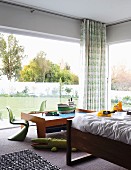 Verglaste Zimmerecke mit teilweise sichtbarem Bett und Klassiker Kinderstühle in Grün um niedrigen Spieltisch mit Modellschiffen