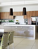 Chairs with patterned covers in front of counter with frosted glass panels and custom fitted cupboards with wooden doors on wall