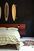 Double bed with wooden headboard and green and white bed linen with pattern of cars below painted skateboards hung on black wall