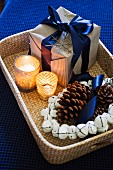 Wrapped Christmas present, tealights, wreath of bells and pine cones on wicker tray