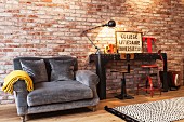 Couch with grey upholstery next to black metal table and vintage swivel chairs against illuminated brick wall