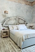 White, antique bedroom with marbled walls, worn wooden floor and reclaimed wooden elements used as bed headboard