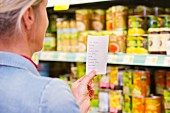 A woman with a shopping list in front of a shelf in a grocery store