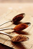 Cinnamon, paprika and cocoa on three silver spoons on a wooden surface