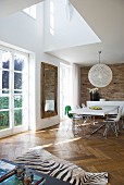 Double-height ceiling in open-plan living area with zebra-skin rug on herringbone parquet floor; dining area with classic chairs and spherical lampshade