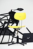 Yellow, retro swivel chair in front of tangle of toppled black wooden stools