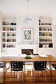 Esstisch und Designerstühle vor offenem Kamin zwischen Bücherregalen in restauriertem Wohnraum mit Stuckdecke