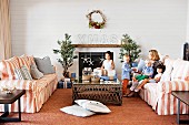 Australische Familie feiert Weihnachten - gestreifte Sofagarnitur und Couchtisch vor offenem Kamin mit Weihnachtsdeko