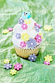 A lemon cupcake decorated with sugar flowers and a bird