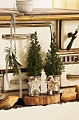 Small fir trees in tin cans decorated with Christmas baubles on wooden board in front of vintage kitchen cooker