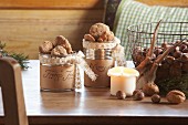 Christmas biscuits in tin cans and white candle next to wire basket of nuts on table