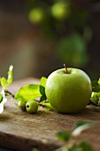 A fresh Granny Smith apple and a sprig from an ornamental apple tree on a wooden board in a garden