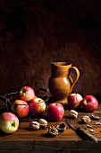 An arrangement featuring apples, walnuts, an earthenware jug and a knife