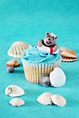 A coconut cupcake decorated with a swimming teddy bear surrounded by seashells