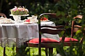 Romantisch gedeckter Kaffee-Gartentisch mit weißer Tischdecke und gepolsterten Holzstühlen mit nostalgischen Flair