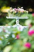 Festliche Blumendekoration auf Glas-Tortenplatte im Freien