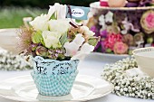 Romantischer Tischschmuck mit Blüten und Namenskärtchen auf Gartentisch gedeckt für festliches Kaffeekränzchen