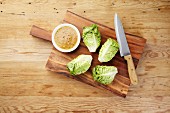 Cos lettuce with a bowl of mustard dressing and a large knife on a wooden board
