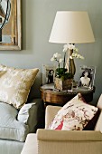 Photos, orchid and lamp with lamps shade on side table between two armchairs