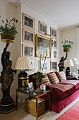 Gilt-framed, historical paintings above red velvet sofa flanked by antique tray supports with pots of lavender