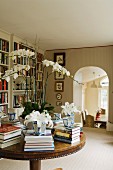Kreisförmig mit Bücherstapeln und weisser Orchideenpflanze belegter Antiktisch in elegantem Bibliotheksraum