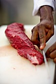 A cook removing the fat from a slice of beef