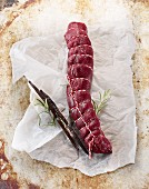 Raw saddle of venison with rosemary and vanilla pods on a piece of paper