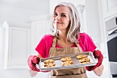 Frau zeigt Backblech mit frisch gebackenen Chocolatechip Cookies