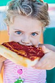 A little girl taking a big bite from a slice of pizza