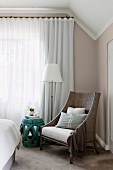 Armchair, side table and standard lamp in front of closed curtains in elegant bedroom