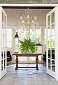 View though open double doors of lanterns on antique table below traditional chandelier with small, white lampshades