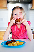 A little girl eating a chicken leg with chips