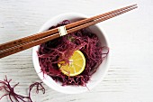 Red seaweed with yuzu slices in a white bowl with chopsticks