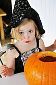 Kleines Mädchen im Halloween-Kostüm mit Kürbis