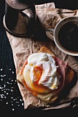 A bird's-eye-view of ham and cheese on toast topped with a poached egg on a piece of paper served with a cup of coffee