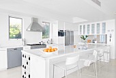 White glossy counter, bar stools and stainless steel fitted appliances in designer kitchen