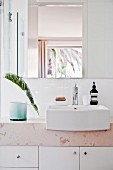 Modern washstand with stone top, base cabinets, white countertop sink and palm frond in vase