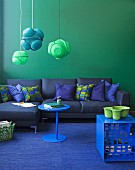 Blue and green colour scheme - blue sofa with scatter cushions against green wall, pendant lamps made from painted colanders and green bowl on blue stool