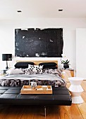 Schwarze Leder Tagesliege vor Doppelbett, seitlich weisser Hocker auf Dielenboden in modernem Schlafzimmer mit schwarzem modernem Bild an Wand