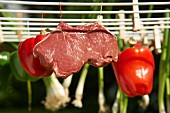 A raw pork steak and vegetables hanging on a washing line