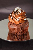 A chocolate cupcake decorated with silver pearls, grated white chocolate and gold powder